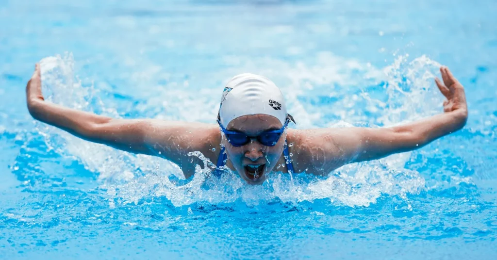 An energetic girl swimming in the pool with safety glasses and cap.