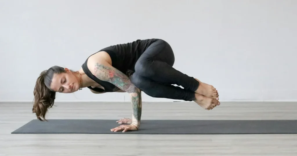 A teen aged girl with tattoos on her arm exercising on a mat.