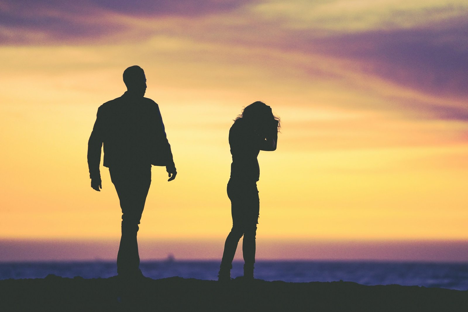 A sunset beach scene featuring the silhouettes of a man and woman, reflecting signs you are stuck in a loveless marriage.