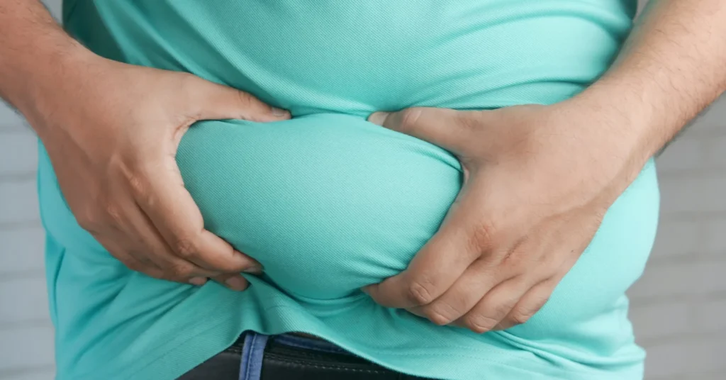 A person folding his belly fat with his hands to show the fat.