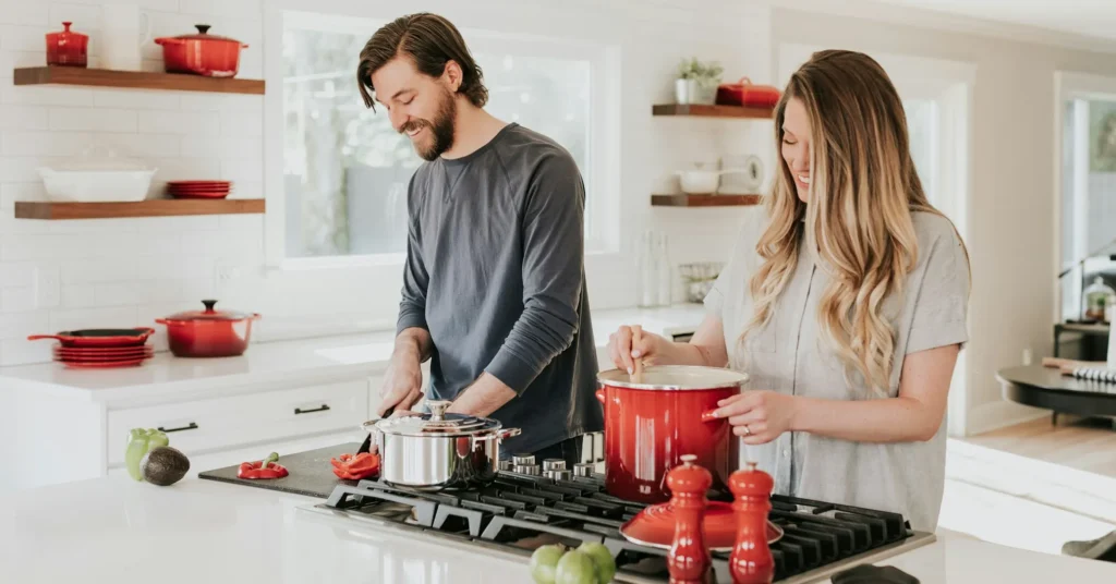 A romantic couple smiling in the kitchen while preparing a dinner.